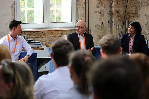 Drei Personen sitzen vor Zuhörern und sprechen mit diesen.