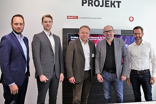 Fünf Männer stehen nebeneinander. Im Hintergrund befinden sich ein Schriftzug Projekt und das Logo von Vodafone.