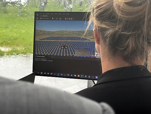 Eine Frau schaut auf einen Bildschirm, auf dem eine simulierte Drohne über einer Solarspiegelanlage schwebt.