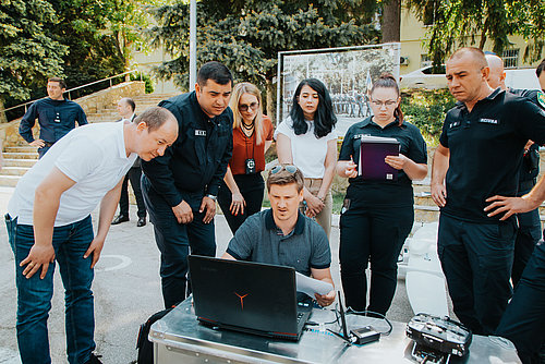 Mehrere Menschen stehen im Kreis um einen Computer. Eine Person erkl&auml;rt Einstellungen am Computer.